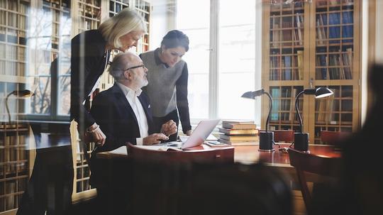 Senior lawyer discussing with female coworkers at table seen through glass in library