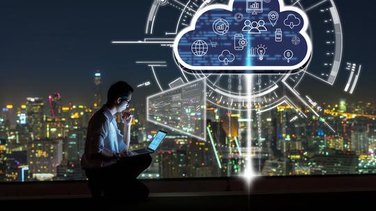 Business success and technology concept, Asian businessman sitting and using the laptop and working with virtual screen connecting with cloud technology over the cityscape background at night time