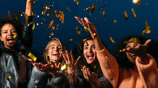 Cheerful Female Friends Throwing Confetti At Night