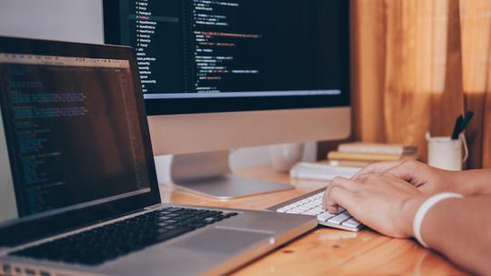 Cropped Image Of Computer Programmer Tying On Keyboard At Desk In Office