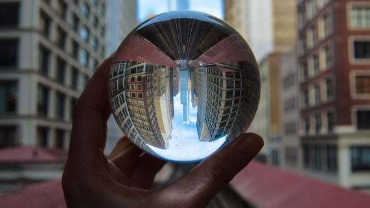 Cropped Hand Holding Crystal Ball With Reflection In City