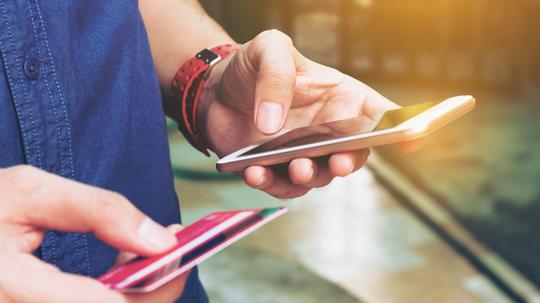 Midsection Of Man With Credit Card Using Smart Phone On Footpath