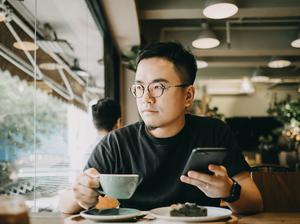 Smart young Asian man using smartphone and having coffee in cafe