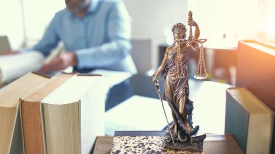 Close-Up Of Lady Justice On Table With Lawyer In Background At Office