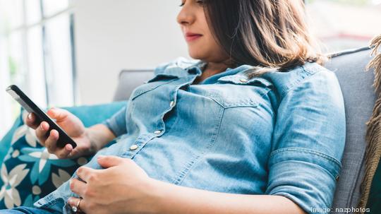 Pregnant woman checking information on smartphone regarding her pregnancy.