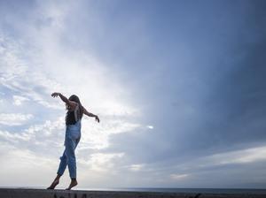 Woman with arms outstretched balancing on wall in front of sky