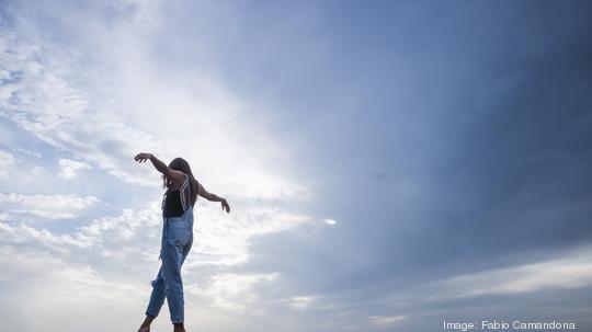 Woman with arms outstretched balancing on wall in front of sky