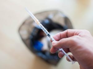 A syringe is being disposed on a trashcan