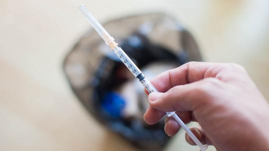 A syringe is being disposed on a trashcan