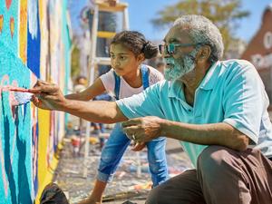 Grandfather and granddaughter volunteers painting vibrant mural on sunny urban wall