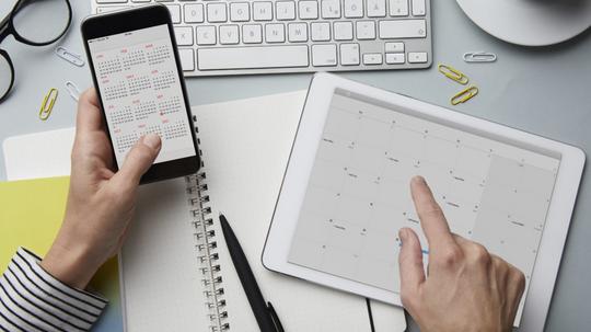 Top view of woman holding smartphone and tablet with calendar on desk