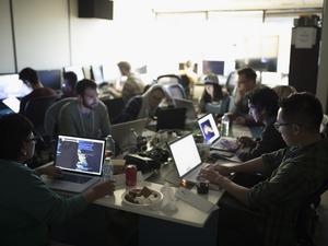 Hackers working hackathon at laptops in dark office