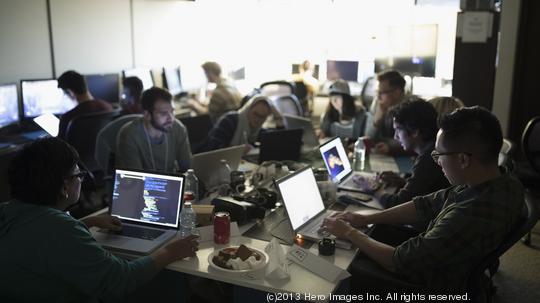 Hackers working hackathon at laptops in dark office