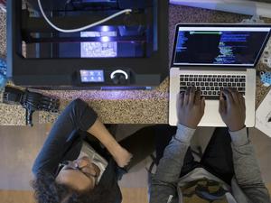 Overhead view designers working at laptop and using 3D printer in office