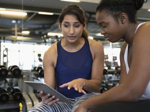 Personal trainer with digital tablet talking with woman in gym