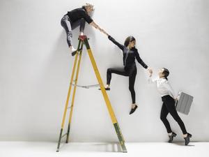 Businesswomen holding hands, helping lift each other on ladder