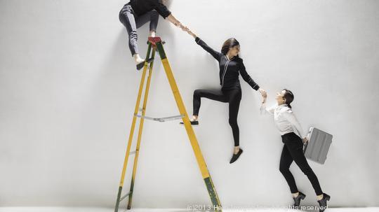 Businesswomen holding hands, helping lift each other on ladder