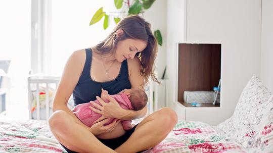 Young mother breastfeeds her baby, holding him in her arms and smiling from happiness