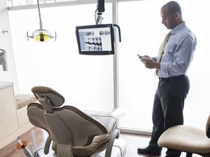 A Middle Eastern male dentist checking his cell phone in a dental examination room