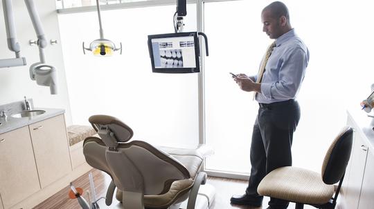 A Middle Eastern male dentist checking his cell phone in a dental examination room