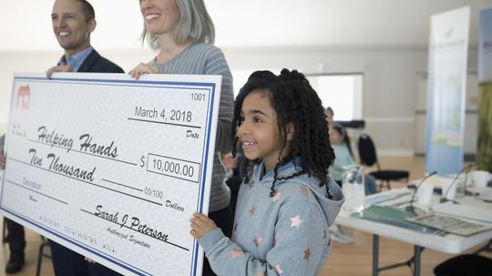 Girl helping hold large donation check in community center