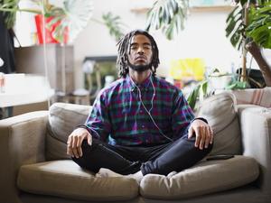 Serene young man meditating with headphones on apartment sofa