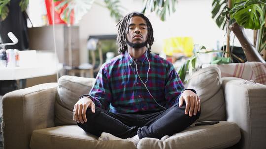 Serene young man meditating with headphones on apartment sofa