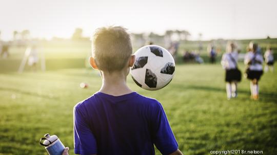 11 year old boy juggling soccer ball while walking off soccer field