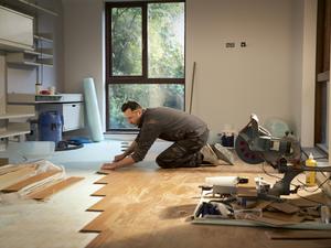 Construction worker laying hardwood flooring in house