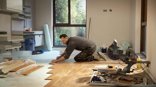 Construction worker laying hardwood flooring in house