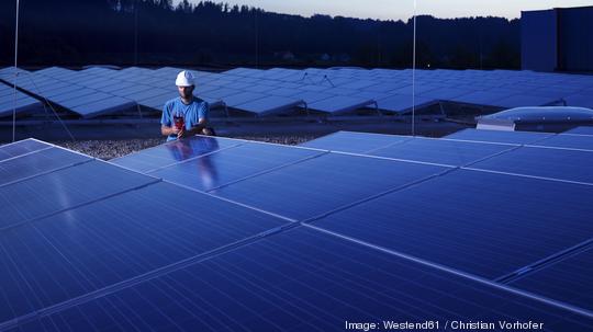 Worker with measuring device checking solar plant in the evening