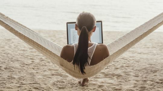 Rear view of woman using laptop computer while relaxing on hammock