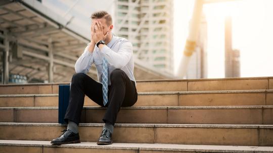 Young business man crying abandoned lost in depression sitting on ground street concrete stairs suffering emotional pain, sadness, looking sick in grunge lighting