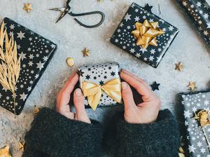 Female hands holding Gift boxes wrapped in black and gold paper on vintage background.