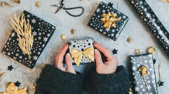 Female hands holding Gift boxes wrapped in black and gold paper on vintage background.