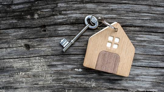 key with shaped house keychain on chain on wood texture background. Idea: buying a house, renting, selling real estate. Mortgage.