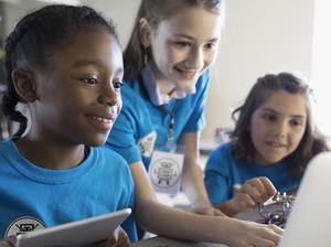 Pre-adolescent girls programming electronics at laptop and digital tablet in classroom