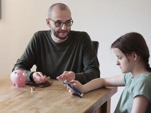 Father trying to discuss savings with teenage daughter who is distracted using mobile phone