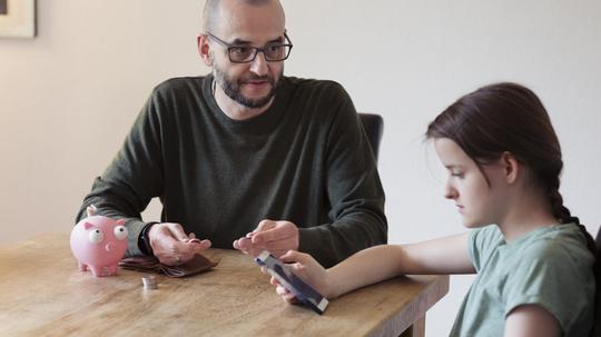 Father trying to discuss savings with teenage daughter who is distracted using mobile phone