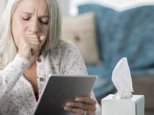 Senior woman coughs while having telehealth appointment on digital tablet with her doctor