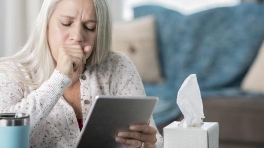 Senior woman coughs while having telehealth appointment on digital tablet with her doctor