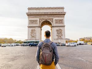 Tourist with backpack walking towards Arc de Triomphe in Paris, France