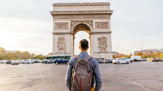 Tourist with backpack walking towards Arc de Triomphe in Paris, France