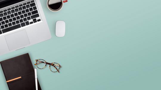 High Angle View Of Laptop With Book And Eyeglasses On Blue Table