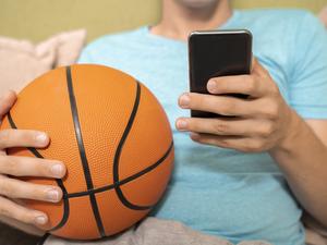 Unrecognizable person holding basketball ball and smartphone