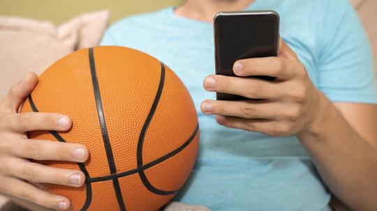 Unrecognizable person holding basketball ball and smartphone