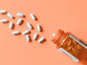 White pills spilling out of prescription bottle onto orange surface