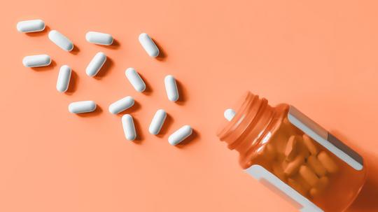 White pills spilling out of prescription bottle onto orange surface