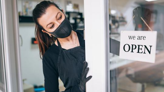 Happy business owner hanging an open sign during COVID-19