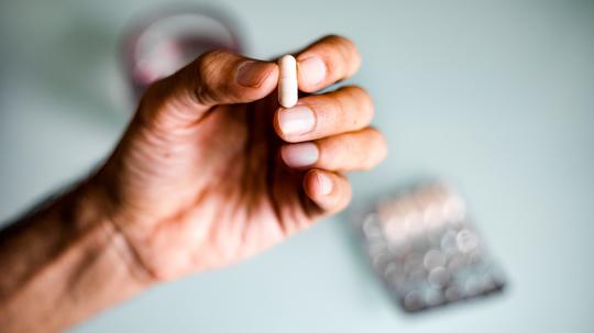 A man's hand holding a capsule / pill